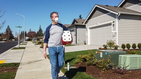 Man wearing a face mask walking through suburbs with toilet paper Stock Footage 128336935