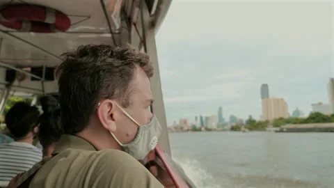 Man wearing face mask while traveling by boat with city skyline in background. Stock Footage 260894310