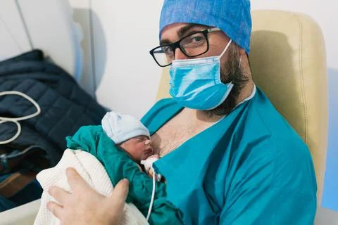 Man wearing face mask while holding his newborn baby in hospital room. Stock Photos