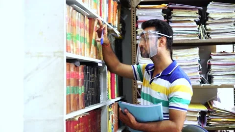 Man wearing face shield busy working in office with lots of books Stock Footage 138261946