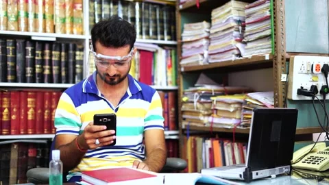 Man wearing face shield  checks his phone sitting in office, New normal, 4k Stock Footage 138251786