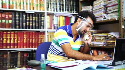 Man wearing face shield talking on telephone while working on laptop in office Stock Footage 138258443