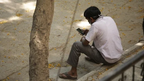 Man-wearing-facemask-sidewalk-smoking-looking-into-his-phone Stock Footage 128722672