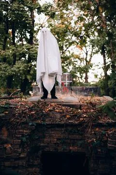 Man wearing ghost costume while standing on the grave in the cemetery during  Stock Photos