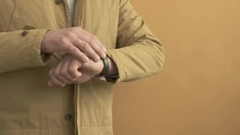 Man wearing ginger colored coat and checking time on a wrist watch Stock Footage 242419275