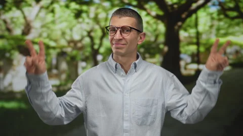 Man wearing glasses in park expressing sarcasm with air quotes and casual a.. Stock Footage 311925197