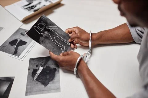 Man wearing handcuffs looking at evidence pictures during interrogation Stock Photos