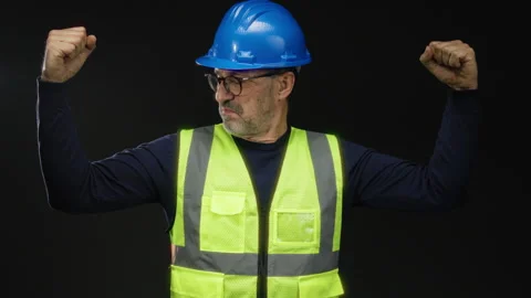 Man wearing hard hat and reflective vest flexing muscles against black back.. Stock Footage 310062086