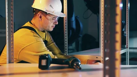 Man wearing hard hat assembles the industrial storage shelf rack Stock Footage 145831269
