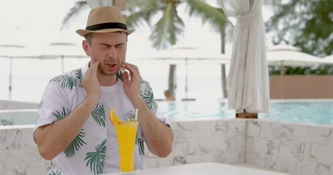 Man wearing hat sitting poolside with tropical drink, experiencing Stock Footage 314043662