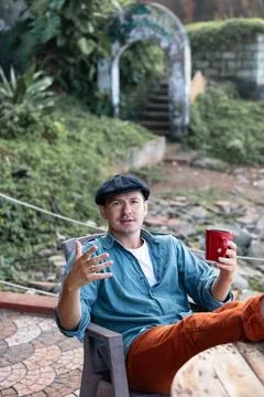 The man wearing a hat is talking while sipping coffee from a red mug Stock Photos