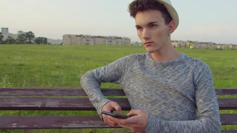 Man, wearing a hat, using his mobile phone, pensive look, sitting on a bench Stock Footage 306237372
