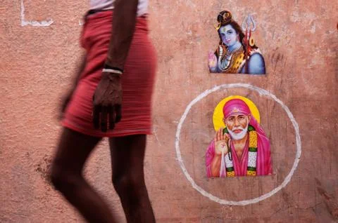 A man wearing a lunghi passes religious pictures on a public wall in Ram Jula Stock Photos