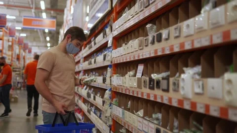 The man wearing mask and choosing outlets, sockets, switches and other Stock Footage 182525053