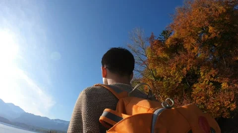 A man wearing an orange backpack is walking along a path near a body of water Stock Footage 314273488