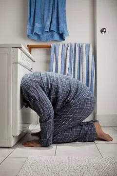 A man wearing pajamas with his head inside a washing machine Stock Photos
