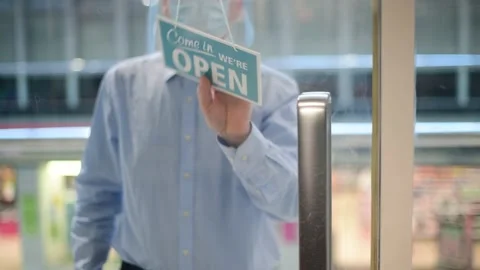 Man wearing protective face mask putting closed shop sign to open uk Stock Footage 142514218