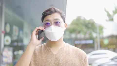 A man wearing a protective face mask walks and talks on the phone in a building. Video stock 252071634