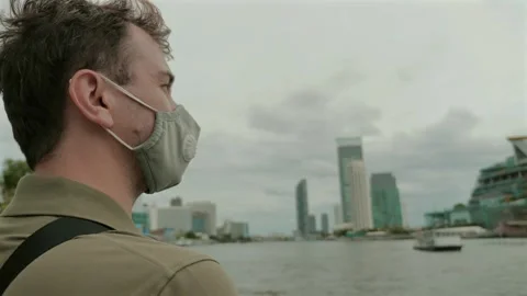 Man wearing protective face mask overlooking cityscape from waterfront Video stock 257889757