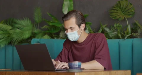 Man wearing protective mask working distantly in cafe.Young guy sitting with cup Stock Footage 164600334