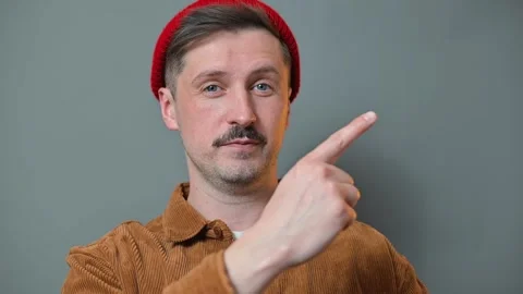 A man wearing a red beanie and brown jacket points in various directions while 動画素材 337642764