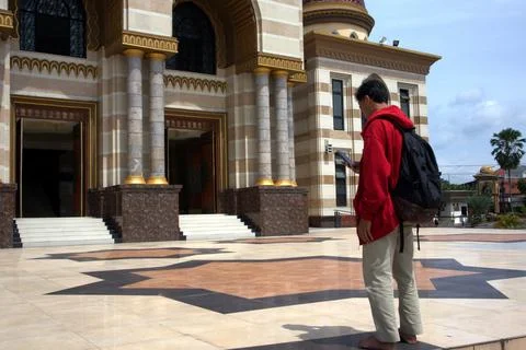 A man wearing a red jacket and carrying a bag visited a beautiful mosque Stock Photos