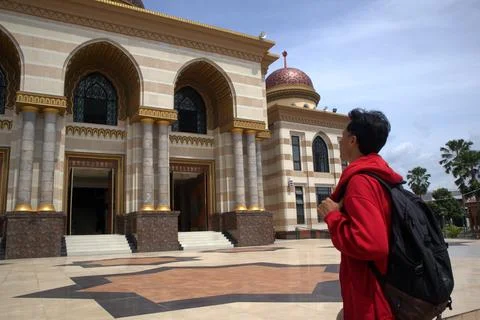 A man wearing a red jacket and carrying a bag visited a beautiful mosque Stock Photos