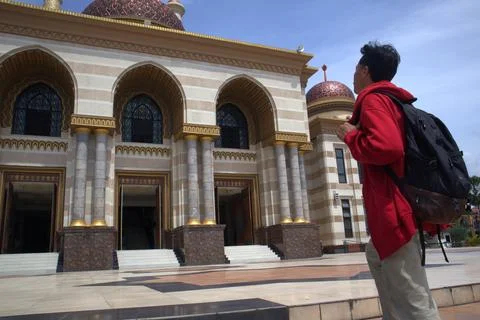 A man wearing a red jacket and carrying a bag visited a beautiful mosque Stock Photos