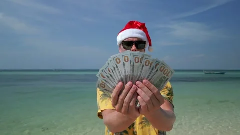 Man wearing Santa hat counting US dollars on tropical beach Stock Footage 258809634