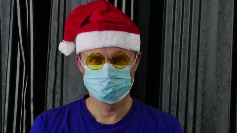 A man wearing a Santa hat, goggles, and medical gloves removes his medical mask. Stock Footage 165772070