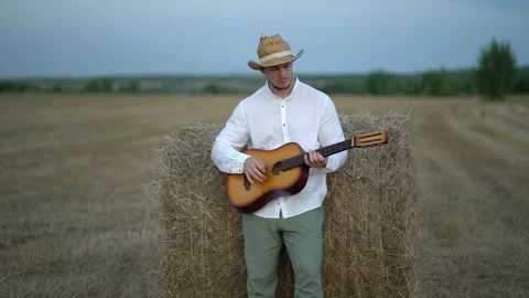 Man wearing a straw hat playing the guitar about a haystack Stock Footage 160437242