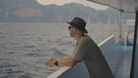 A man wearing a sun hat and sunglasses is lounging on the edge of a boat, gazing Stock Footage 264812965