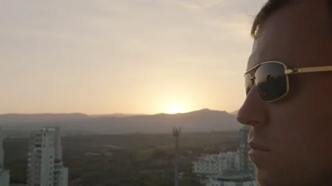 Man wearing sunglasses, the sun is setting behind the mountains Stock Footage 307933267