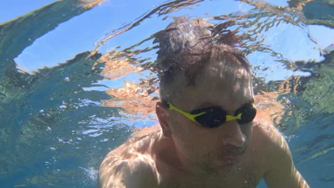 Man wearing swim goggles looking at the camera while floating at the sea surface Stock Footage 344829205