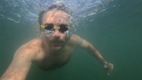 Man wearing swimming goggles exploring underwater, exhaling air bubbles. Stock Footage 343078499