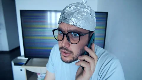 Man wearing a tinfoil hat makes a phone call while expressing disbelief and 스톡 동영상 307824129