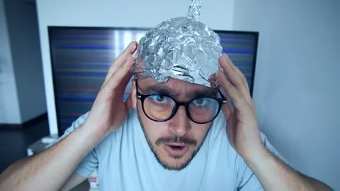 Man wearing a tinfoil hat makes a humorous gesture reflecting conspiracy Stockbeeldmateriaal 307824501