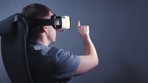 A man wearing virtual reality glasses sits in a chair and clicks on a virtual Stock Footage 115089488