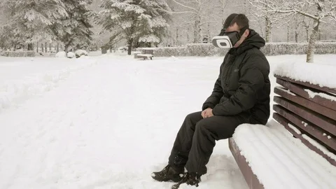 A man wearing a virtual reality headset in the winter in a snowy park. He tries Stock Footage 71222470