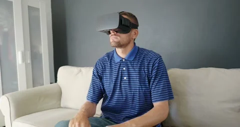 Man wearing virtual reality headset sitting on couch at home. Stock Footage 168373721