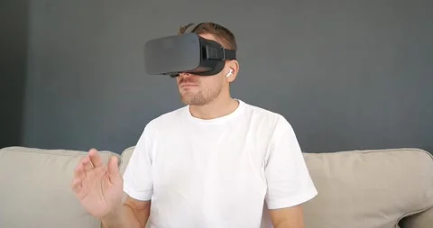 Man wearing Virtual Reality headset, sitting on couch while virtual meeting. Stock Footage 168493404