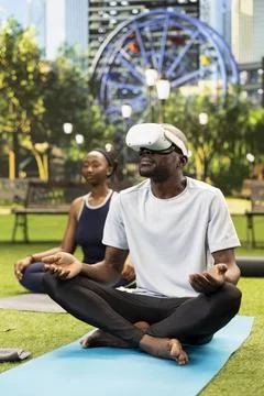 Man wearing virtual reality headset and meditating cross-legged on blue yoga mat Stock Photos