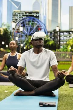Man wearing VR headset and sitting cross-legged on yoga mat in city park Stock Photos