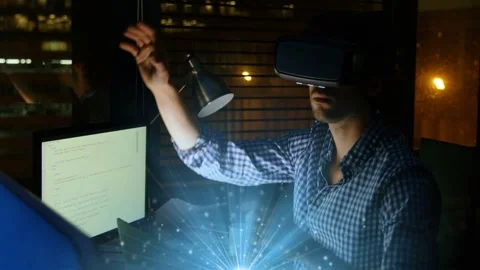 Man wearing VR headset touching chin then reaching blue hologram above desk, Stock Footage 333210937