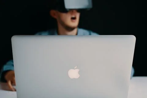 A man is wearing a VR headset while working on a task using a laptop computer Foto stock