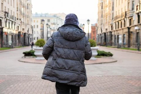 Man wearing warm down jacket walking in city street. Concept of real estate.. Stock Photos