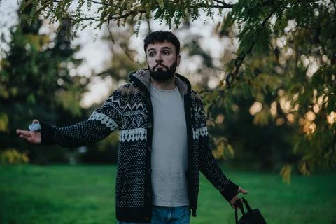 A man wearing a warm patterned sweater stands under tree branches, gesturing Stock Photos