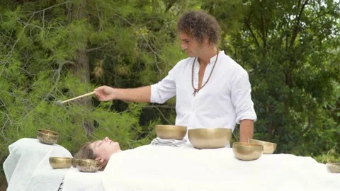 A man wearing in white doing healing sound massage with tibetan singing bowl Stock Footage 213889509