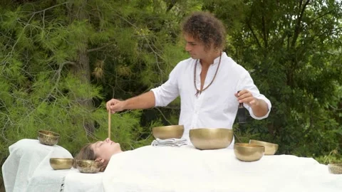 A man wearing in white doing healing sound massage with tibetan singing bowl Stock Footage 213890344