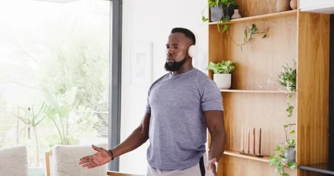 Man wearing white over-ear headphones standing in living room near shelving Stock Footage 342234021